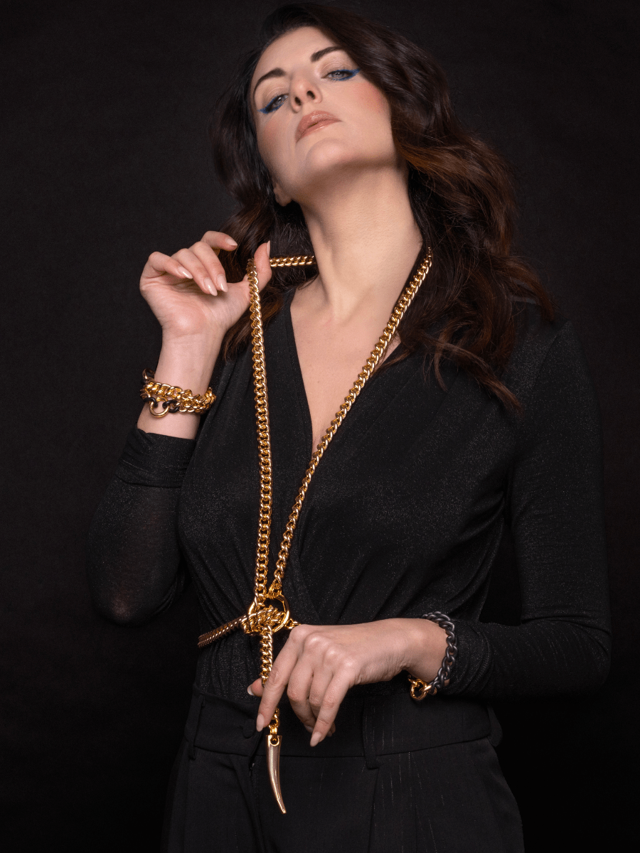 Woman wearing a gold body chain and bracelet against a black background