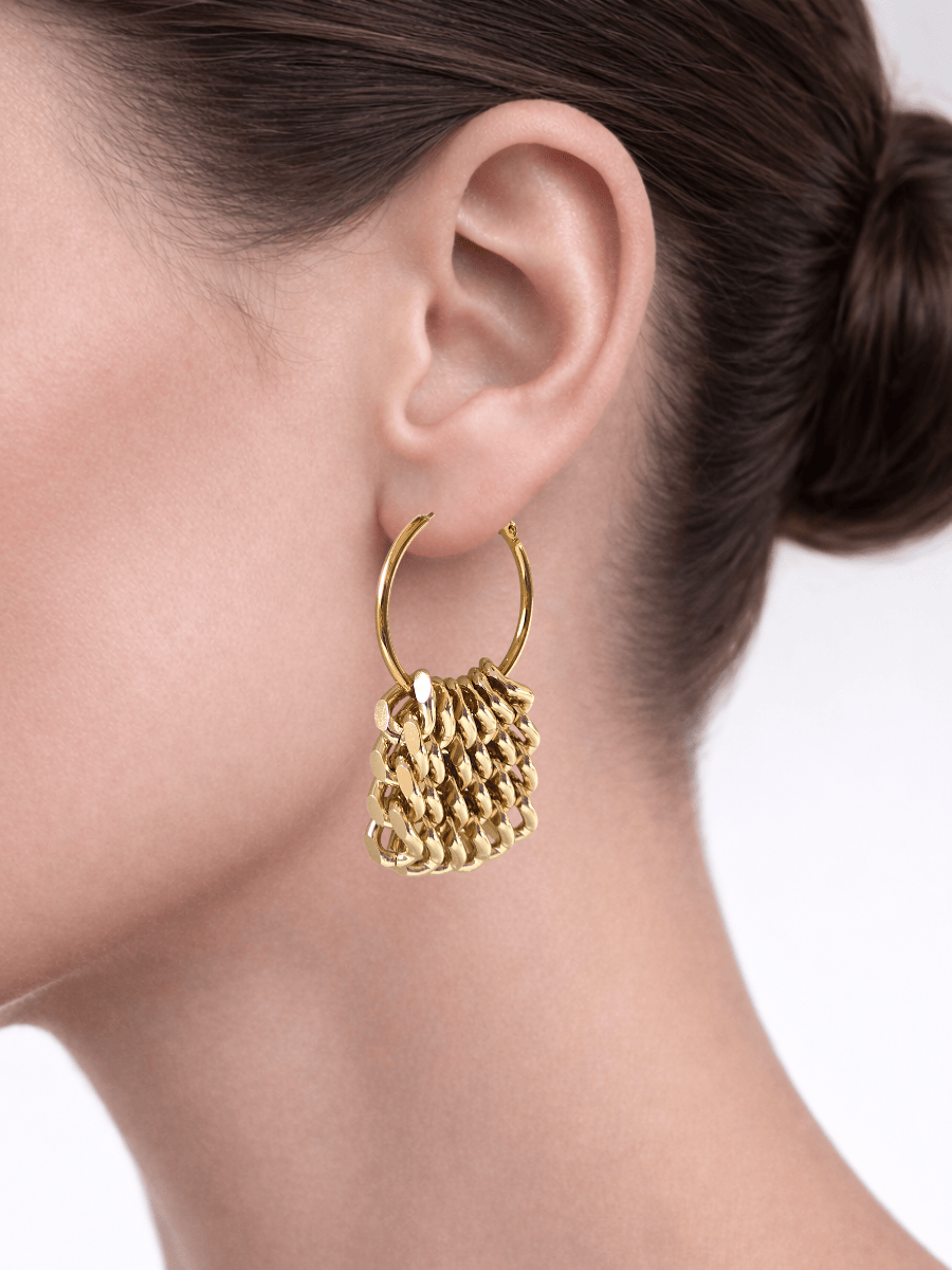 Gold hoop earrings with drop fringe worn by a person on a plain background