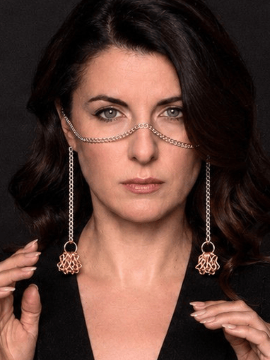 Woman wearing a long tassel face chain against a dark background