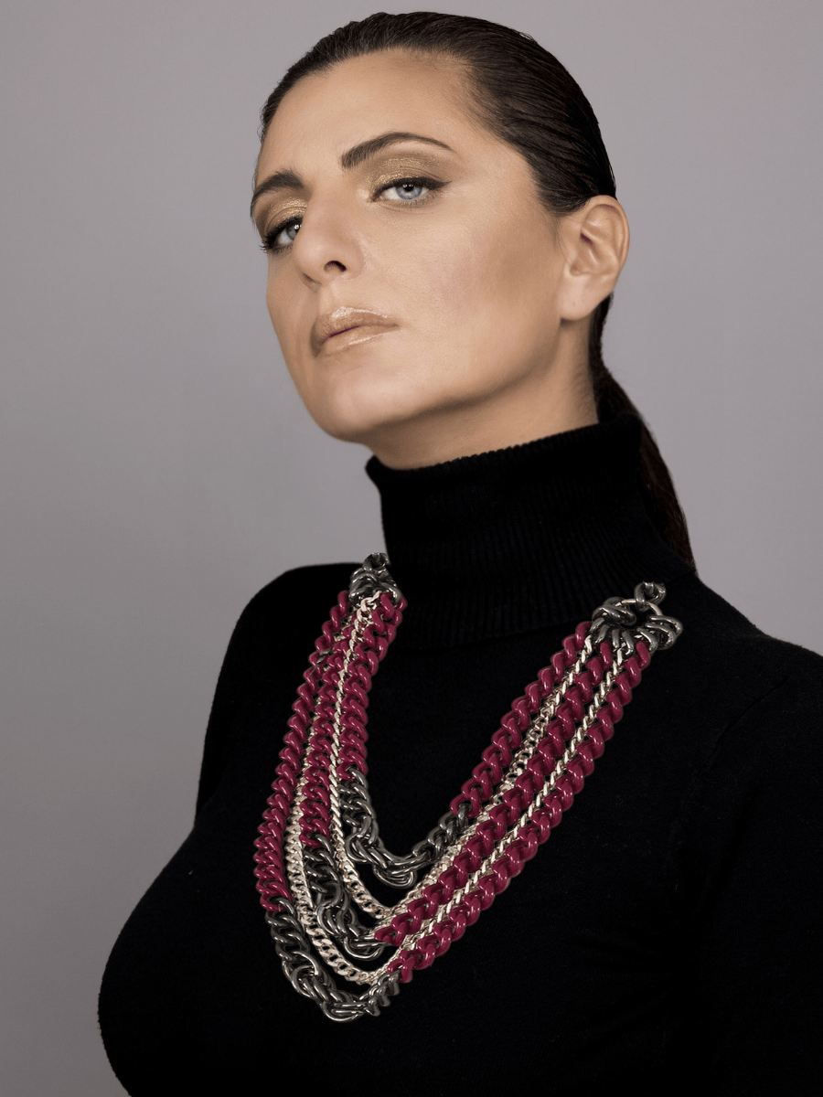 Woman wearing a black turtleneck and aubergine multistrand necklace with a gray background