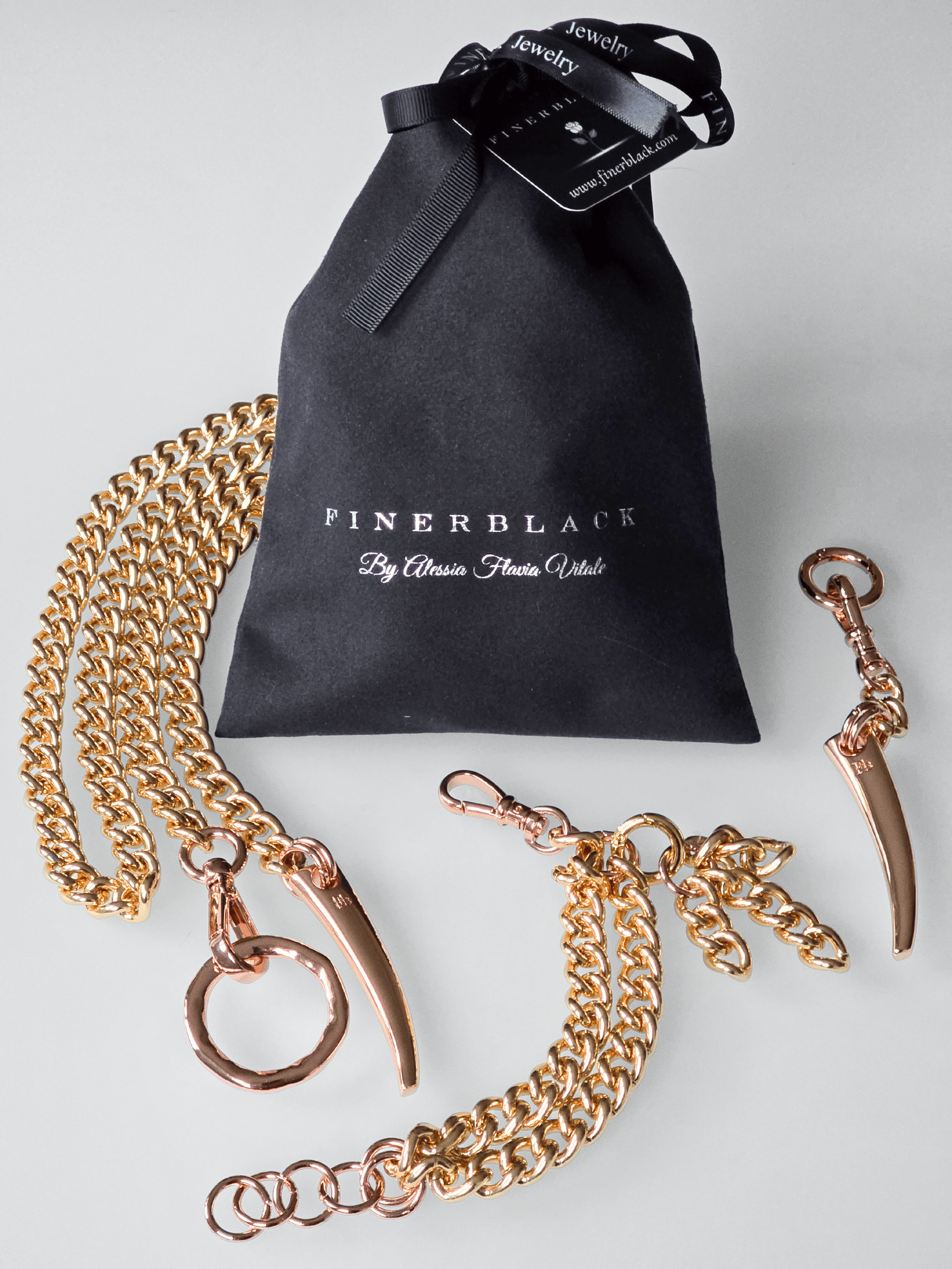Gold chain necklace with rose gold accents, bracelet and keychain set and a black jewelry bag on a light gray background