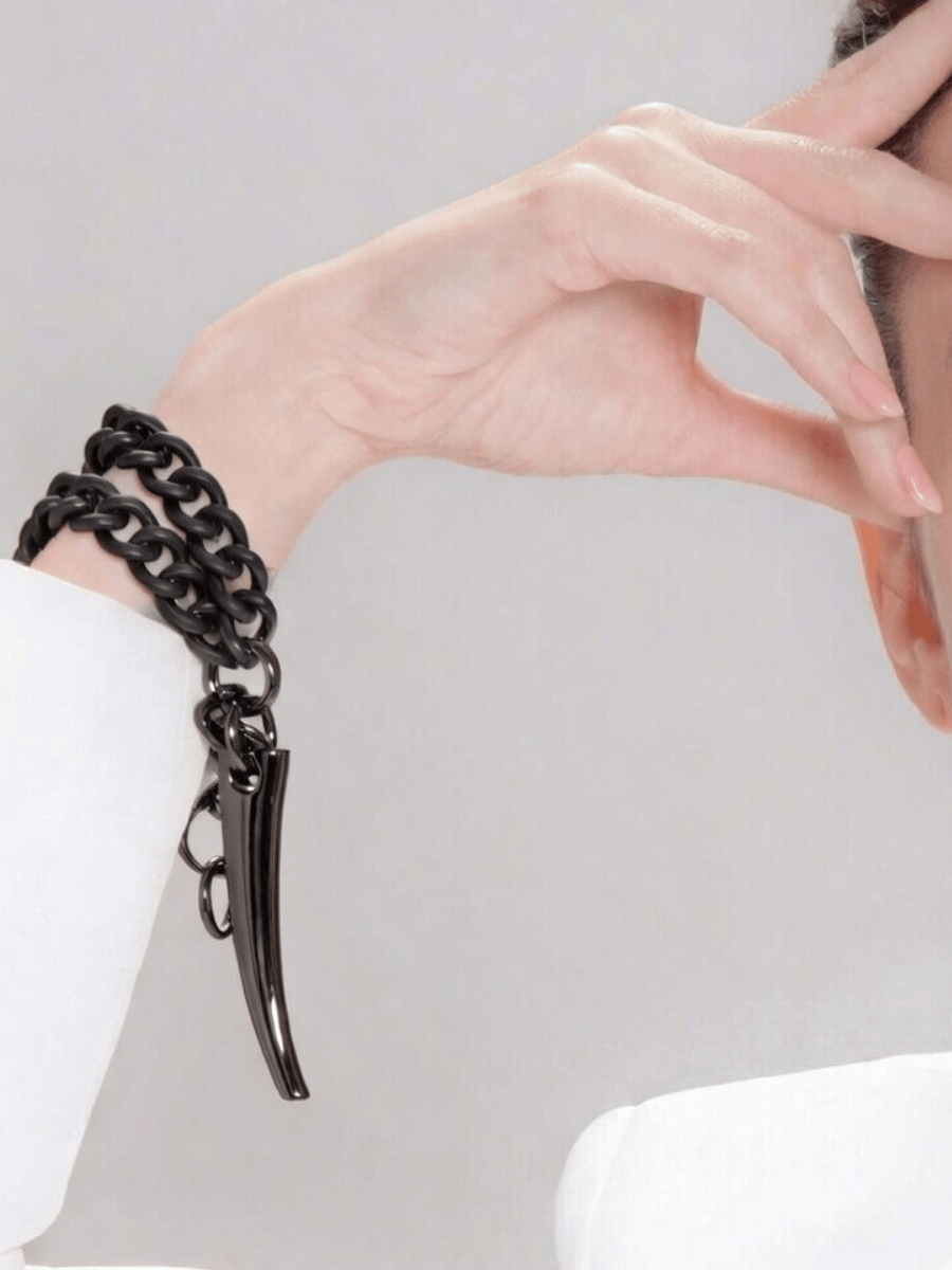 Black chain bracelet with a unique horn pendant worn on a wrist against a light background