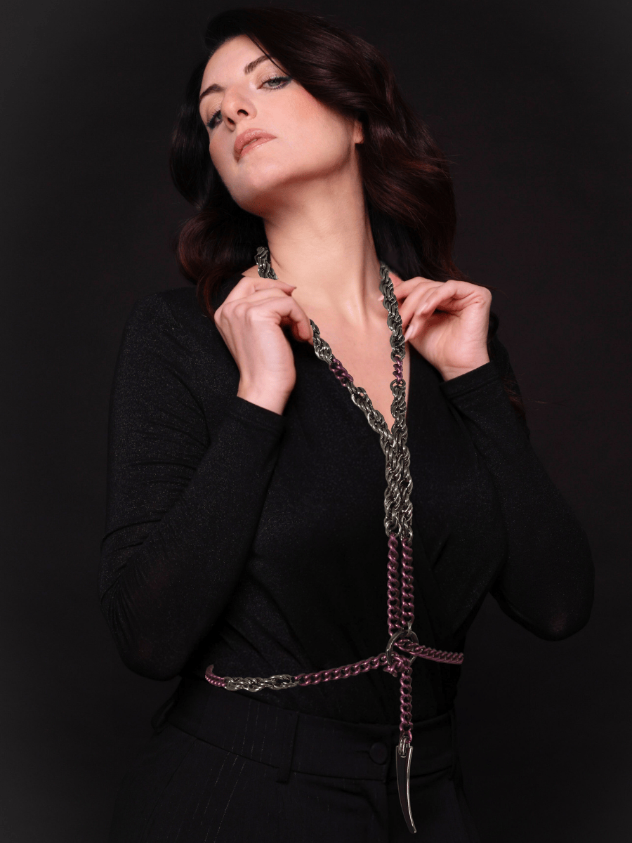 Woman wearing a black outfit with a decorative body chain in purple gunmetal against a dark background
