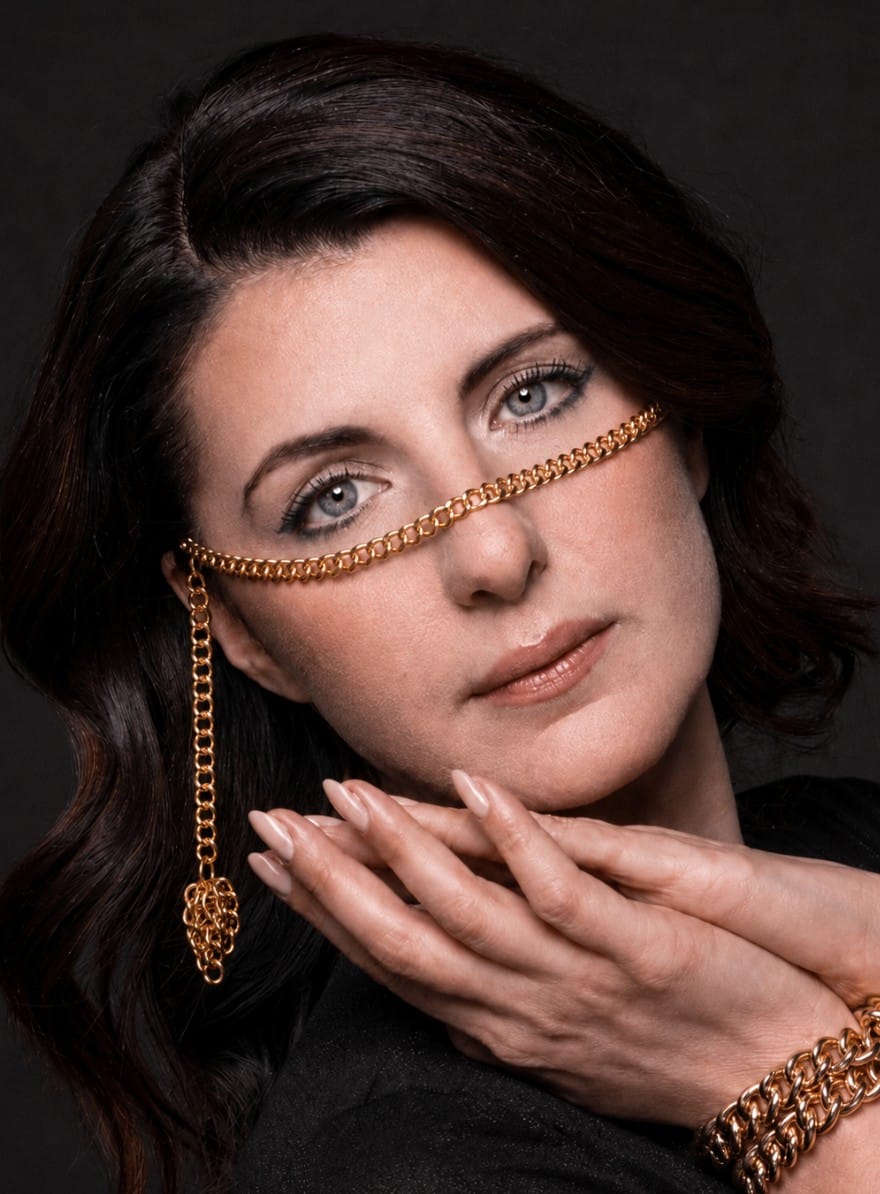 Woman wearing a gold chain on the face against a dark background