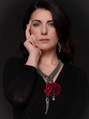 Woman wearing a black top and a necklace with a red rose chain necklace ethnic pendant against a dark background