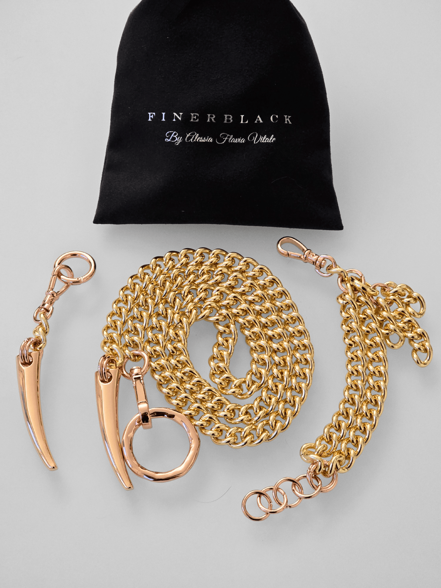 Gold chain with rose gold hardware matching bracelet and keychain set and 'FinerBlack' pouch on a light gray background