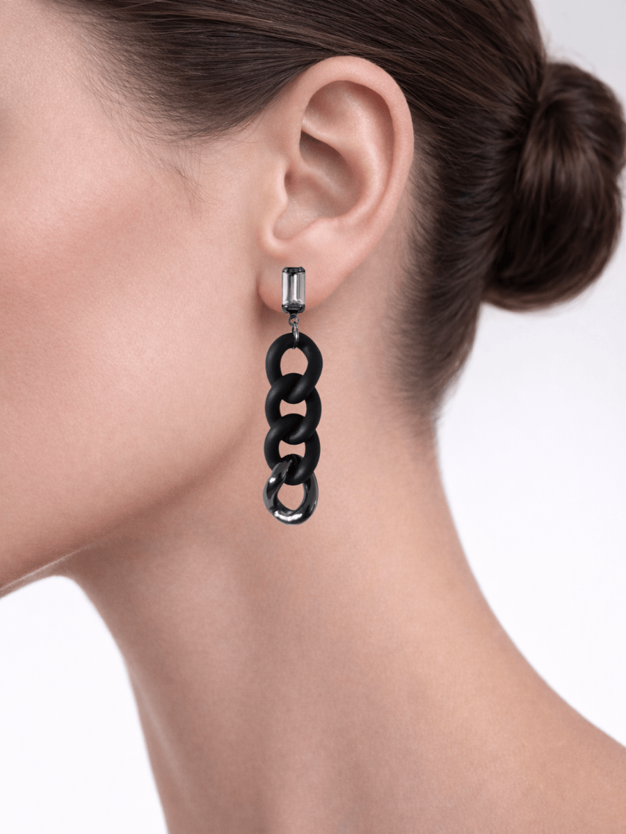 Black chain earring worn by a model on a plain background
