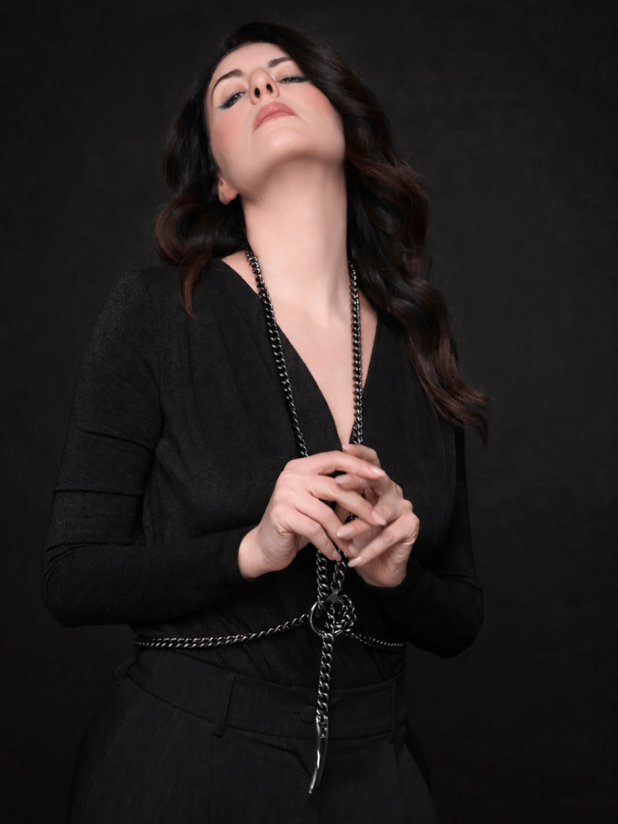 Woman wearing a black outfit with a long body necklace against a dark background