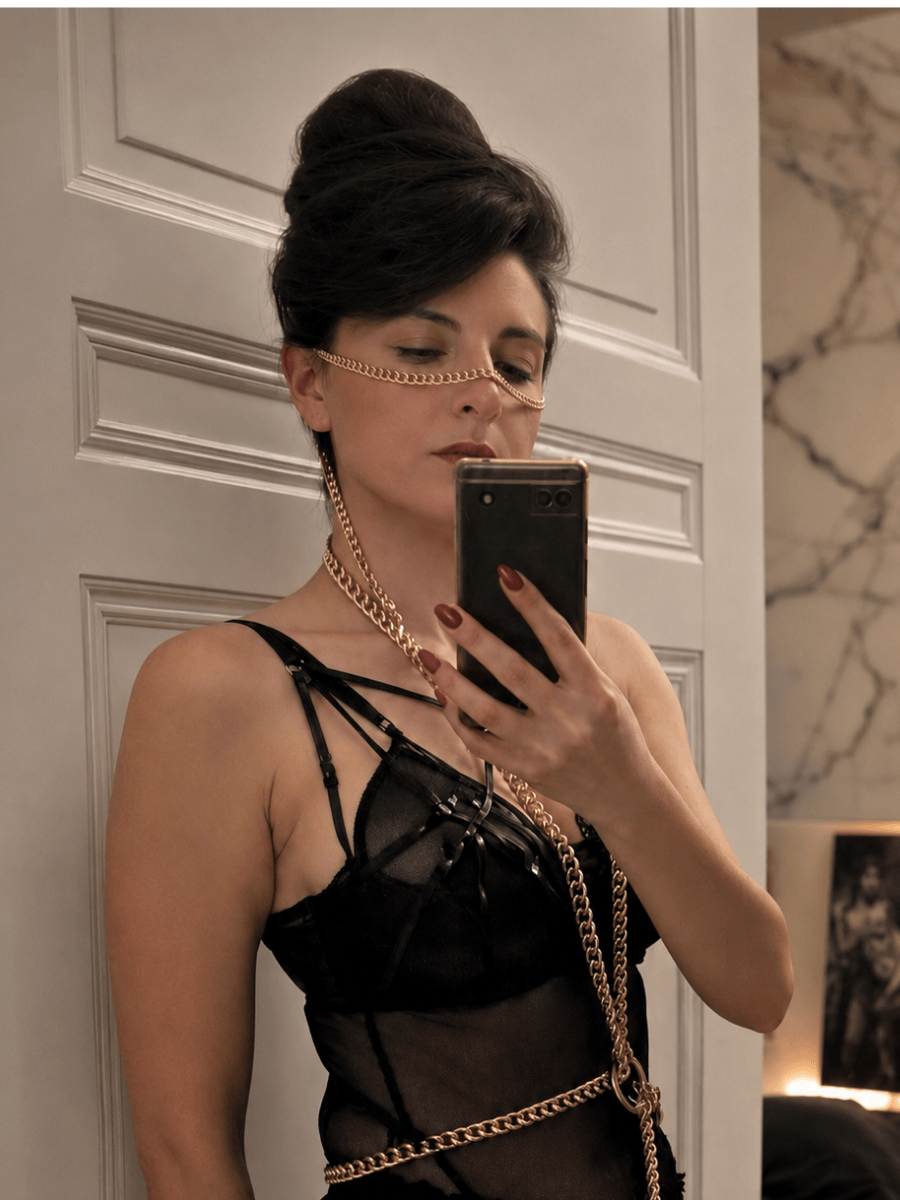 Woman taking a mirror selfie wearing a black outfit with gold chains.