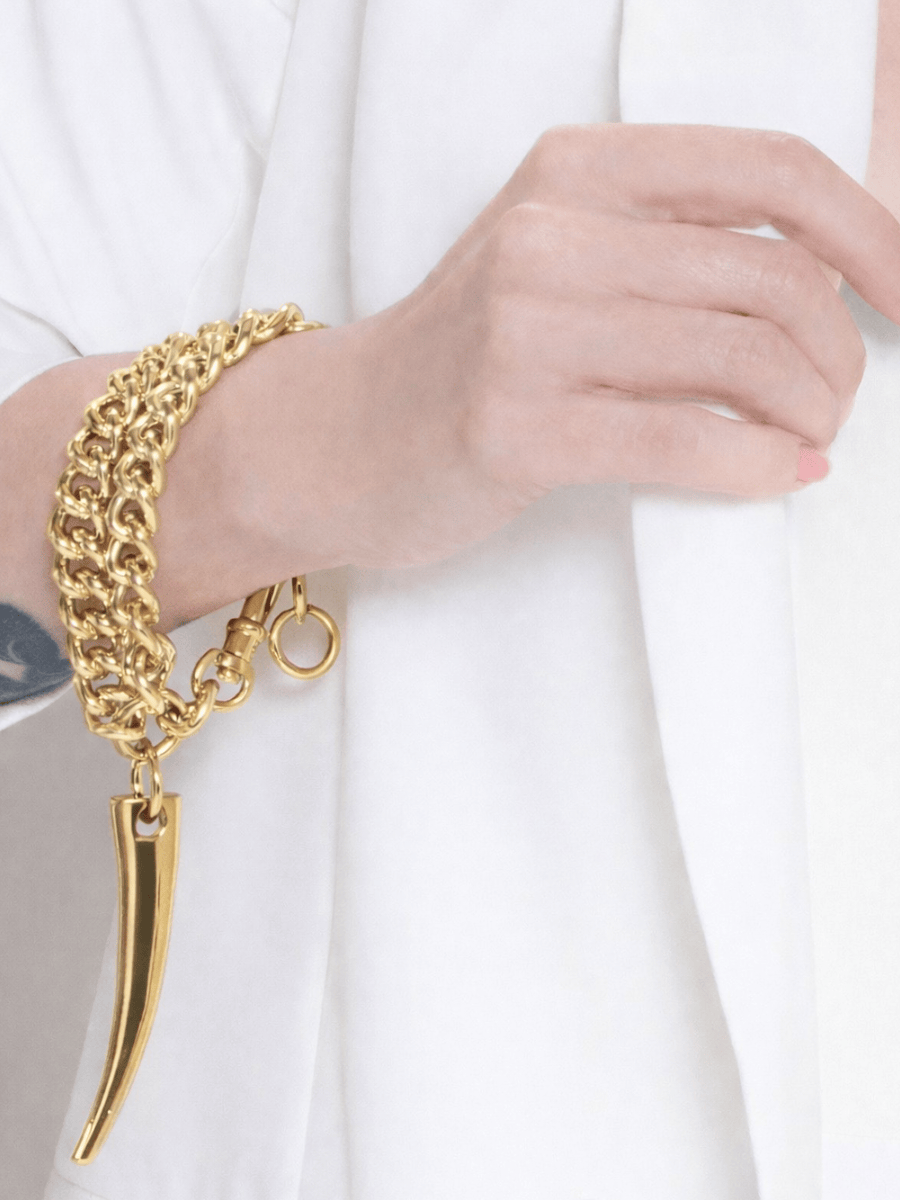 Gold bracelet with a unique big horn pendant design worn on a white background