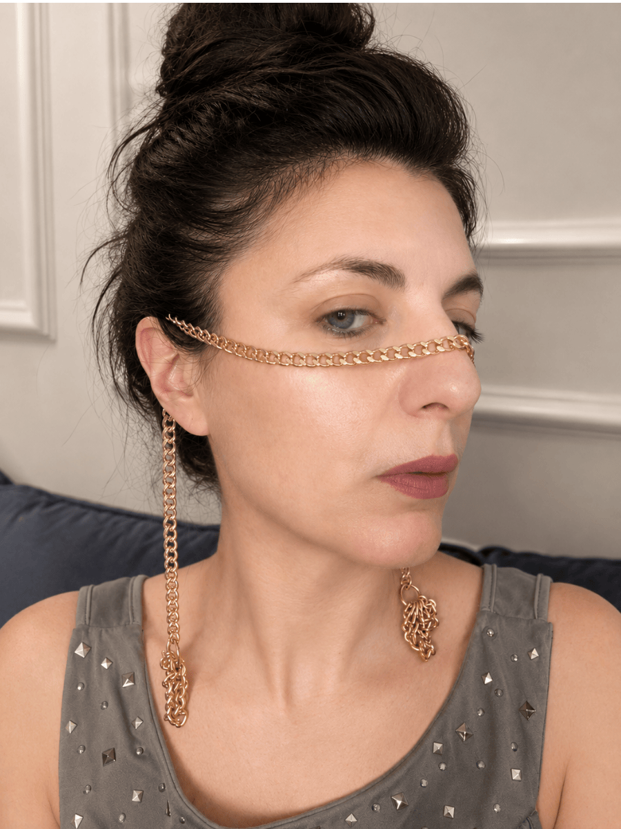 Woman wearing a gold chain with long tassels around her face with a neutral background